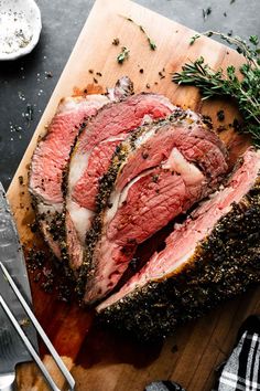 a piece of meat on a cutting board with herbs and seasoning next to it