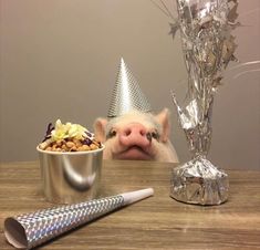 a pig with a party hat sitting at a table next to a bowl of food