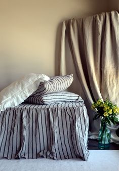 a bed with two pillows on top of it next to a vase filled with flowers