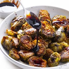 a white bowl filled with brussel sprouts and sauce being drizzled on top