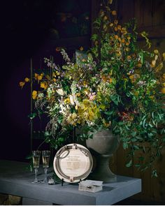 an arrangement of flowers in a vase on a table next to a plate and glasses