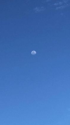 an airplane flying in the blue sky with a moon behind it and some trees on the other side