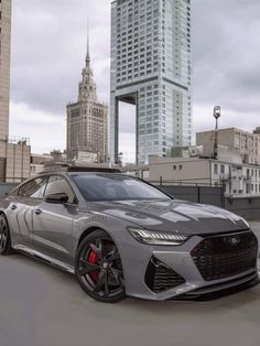 a grey sports car parked in front of tall buildings on a cloudy day with red rims