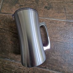 a stainless steel coffee cup sitting on top of a wooden floor