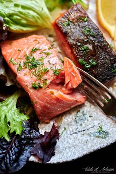 a plate with salmon, lettuce and lemon wedges on it next to a fork