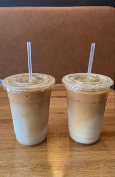 two iced coffees sitting on top of a wooden table with straws in them