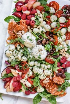 a white platter filled with fruit and veggies on top of a marble table