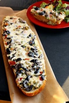 a long piece of bread sitting on top of a table next to a plate of salad