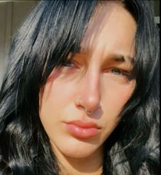 a woman with long black hair and piercings on her nose looking at the camera