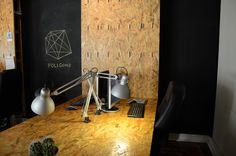 a wooden desk topped with a computer next to a blackboard covered in geometric designs