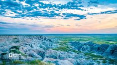 the sun is setting over badlands and rocky hills in the distance, with grass growing on the ground