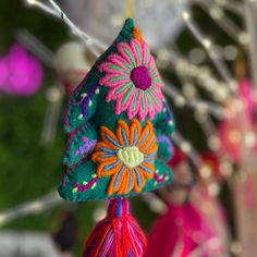 an ornament hanging from a tree decorated with colorful flowers and tassels