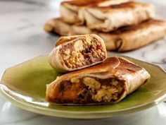 two burritos on a green plate sitting on a marble counter top next to each other