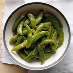 a white bowl filled with green beans on top of a wooden table next to a napkin