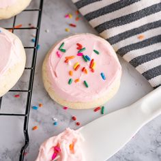 pink frosted cookies with sprinkles on a cooling rack next to a striped towel