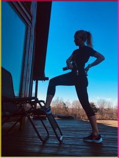 a woman standing on top of a wooden deck next to a chair with her leg in the air