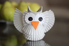 an owl made out of paper sitting on top of a table next to some apples