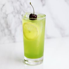 a green drink with a slice of lemon and a cherry on the rim, sitting on a marble surface