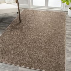 a brown rug in a living room next to a white chair and potted plant