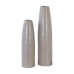 two tall silver vases sitting next to each other on a white surface with no one in it