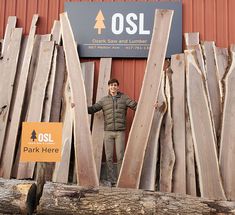 a man standing in front of a pile of wooden planks next to a sign