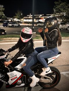 two people sitting on a motorcycle in the middle of the street, one wearing a helmet