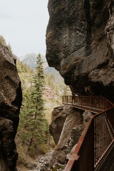 a bridge that is next to a cliff with trees on the other side and mountains in the background