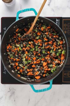 carrots and black beans cooking in a pot on the stove top with a wooden spoon