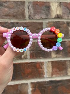 Custom name sunnies surrounded in pearls, with the cutest rainbow smiley face beads. So simple and perfect for everyday wear, or for a fun occasion. Super lightweight! Fully custom - in the personalization box, please write the child's name and which bead color you would like. If not noted, default option is black & white letters. I can also make these on flower frames - just leave me a note in the personalization box! Sunnies best fit 2-8 year olds. *Contains small parts. Though I use industria Pink Personalized Adjustable Sunglasses, Playful Personalized Pink Sunglasses, Cute Personalized Adjustable Sunglasses, Custom Name Pink Sunglasses With Adjustable Fit, Pink Sunglasses With Custom Name And Adjustable Fit, Fun Sunglasses With Gradient Lenses For Gift, Fun Sunglasses With Uv Protection For Gift, Fun Sunglasses With Uv Protection As Gift, Playful Customizable Adjustable Sunglasses