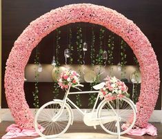 a white bicycle parked under a pink flower covered arch with flowers on the front and side