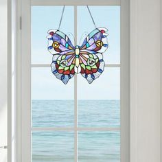 an open window with a stained glass butterfly hanging from it's side and the ocean in the background