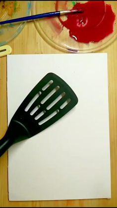 a spatula sitting on top of a piece of paper next to a paintbrush