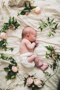 a baby laying on top of a white blanket covered in flowers and greenery next to pink roses