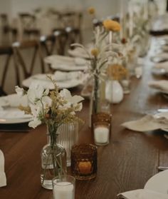 the table is set with white and yellow flowers in glass vases, candles, and napkins