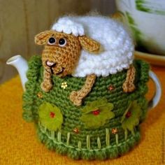 a crocheted sheep sitting on top of a green tea pot