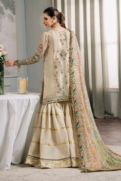 This 3-piece set features a skin colored shirt with intricate handwork on the neckline, made of luxurious masuri fabric adorned with gleaming zari work. The dress is embellished with fancy lace and tilla accents, creating a touch of grandeur. The serene flow of the dress is enhanced by a subtle blend of hues, accompanied by a digitally printed embroidered chiffon dupatta and dyed silk trouser. Custom stitching is available with this product. Upon placing your order, you will receive an email req Gharara Dress, Fancy Laces, Embroidery Goldwork, Nikah Outfit, Pakistani Designer Clothes, Asian Designers, Pakistani Party Wear, Color Skin, Kurta Dress