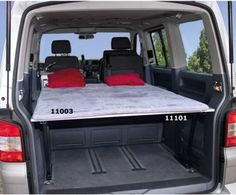 the back end of a white van with two red pillows on it's bed