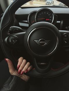 a woman holding the steering wheel of a mini cooper countryman with red stitching