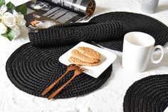 two cookies on a white plate next to a coffee cup and utensils with black braided placemats