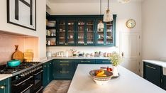 a bowl of fruit is on the counter in this kitchen with blue cabinets and white counters