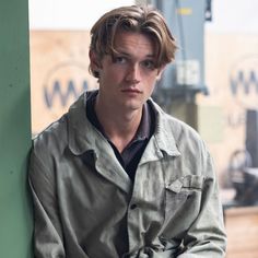 a young man leaning against a green wall