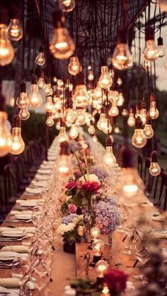 a long table with lots of lights hanging from it's ceiling and flowers in the center