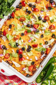 a casserole dish filled with mexican food and vegetables on a colorful table cloth