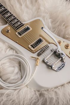 a white electric guitar laying on top of a fur covered floor next to a charger