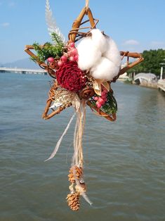 a bouquet of flowers and cotton hanging from a rope by the water's edge