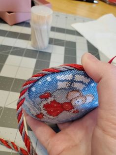 a hand holding a piece of fabric with a bear on it and red string attached to it