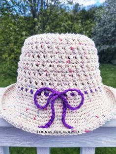 a crocheted hat with a purple bow on it sitting on a wooden bench