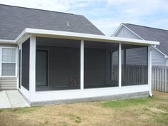 a house that is sitting in the grass next to a fence and some houses with windows