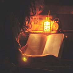 a woman reading a book in the dark with an alarm clock on the wall behind her