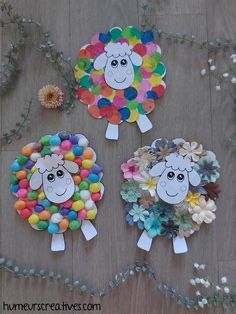 three sheep made out of paper plates on a wooden floor with flowers and leaves around them